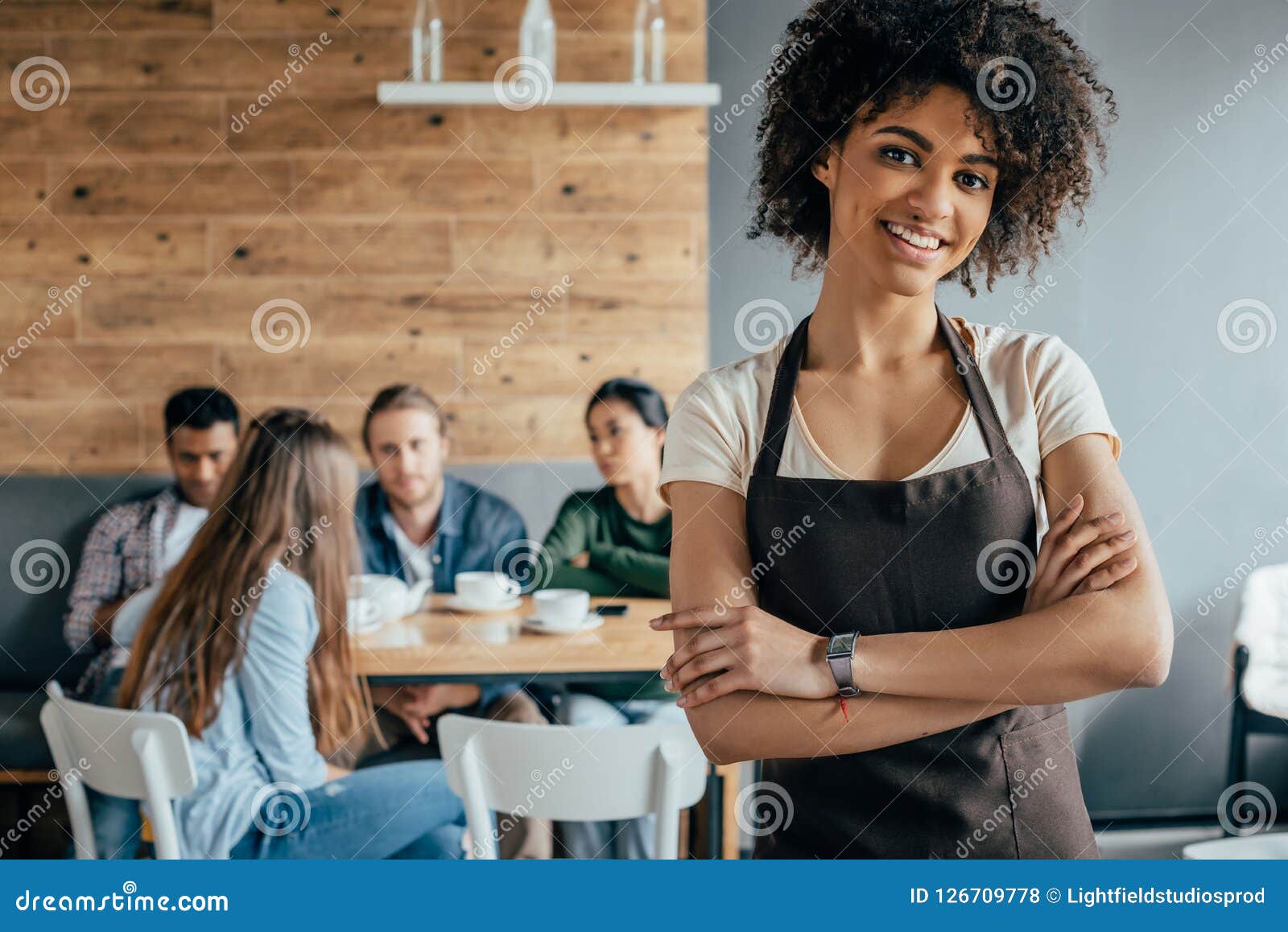 smiling african american waitress standing with customers sitting behind