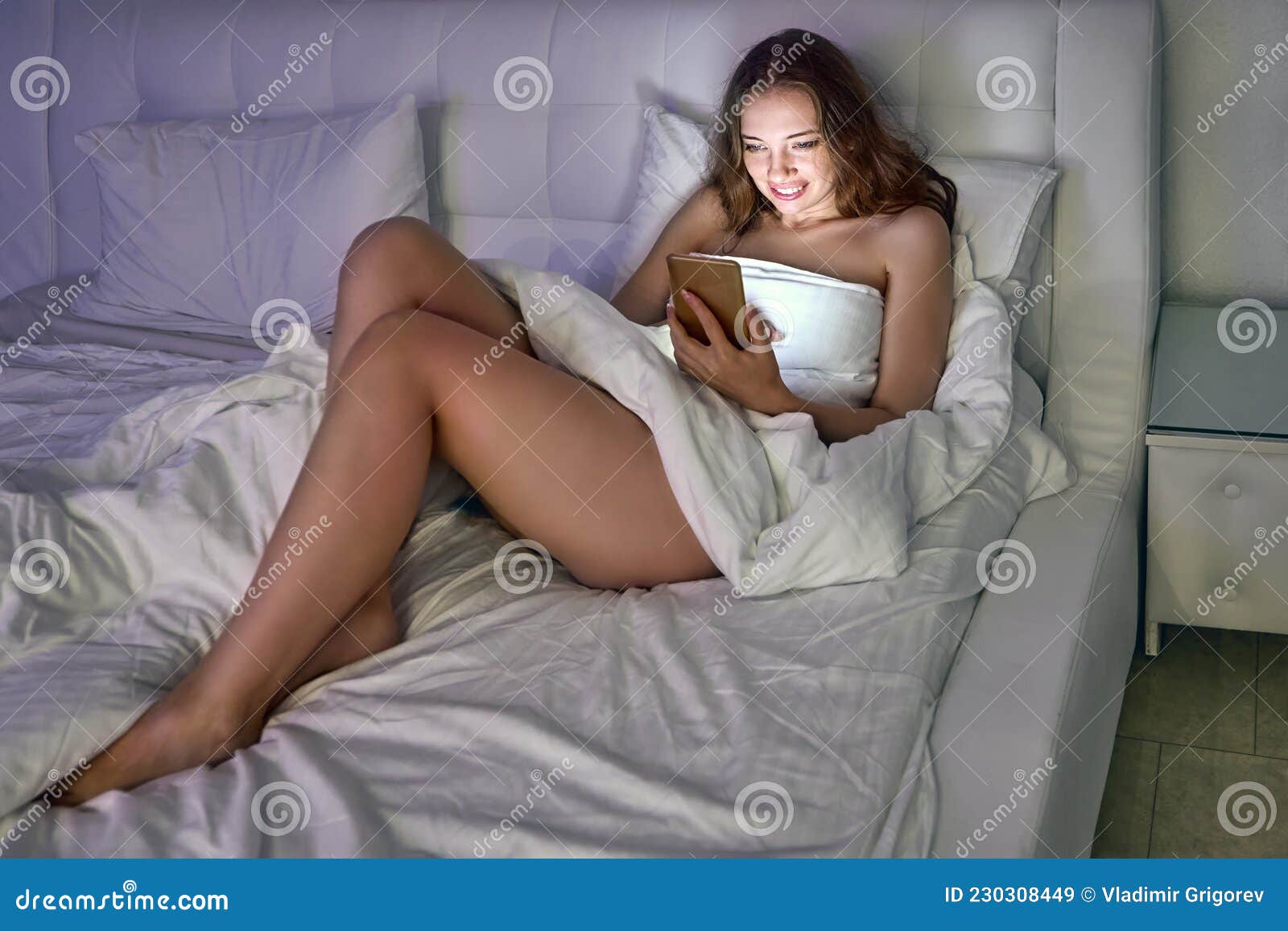 Happy Naked Woman Lies in Bed with Smartphone and Chatting with Friends