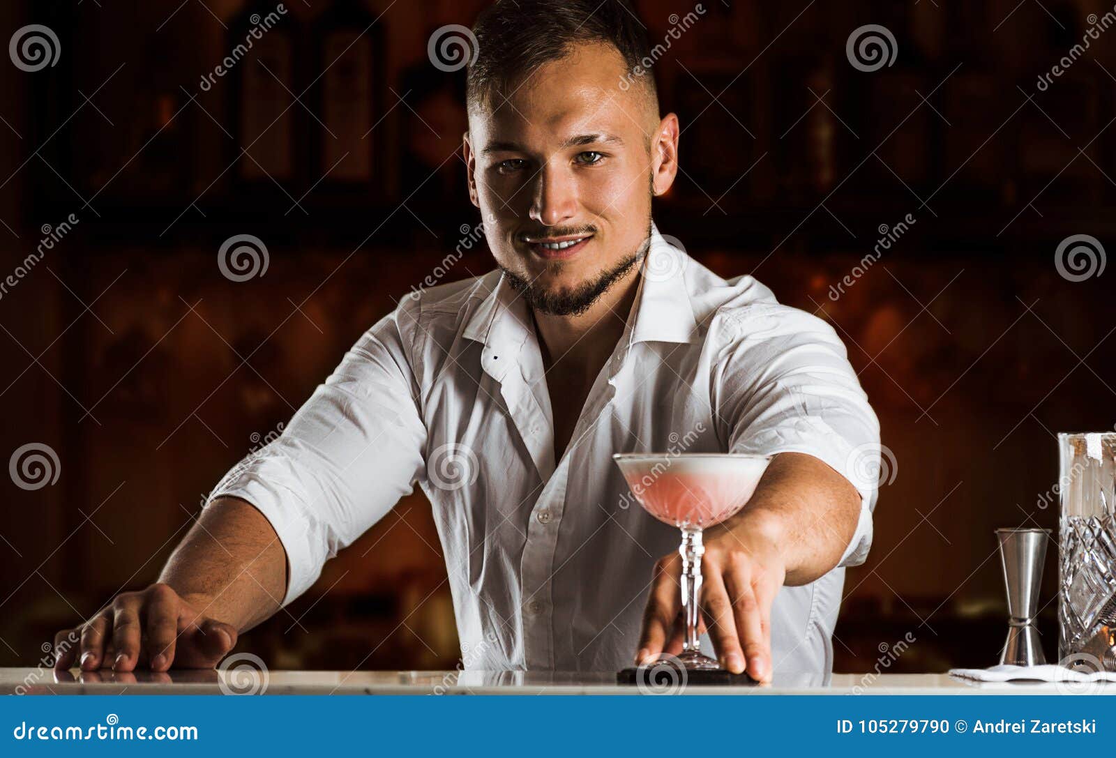 smiling bartender gives the guest a chic cocktail in a tall glass.