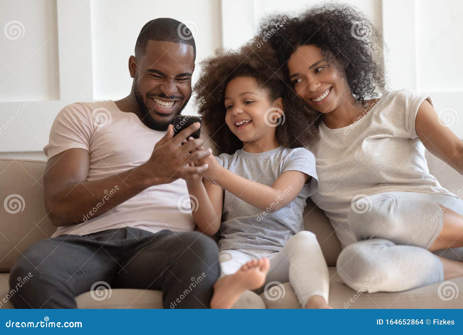 smiling biracial family with kid laugh enjoy video on cell