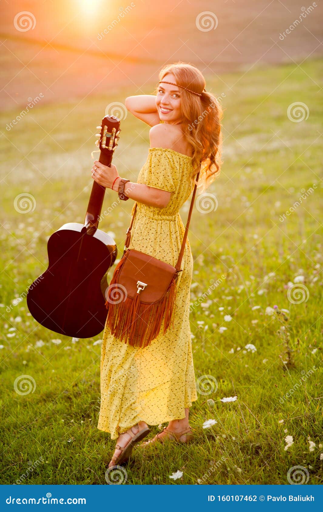 Beautiful Hippie Girl With Guitar On Field Sniffing A Flower At Sunset