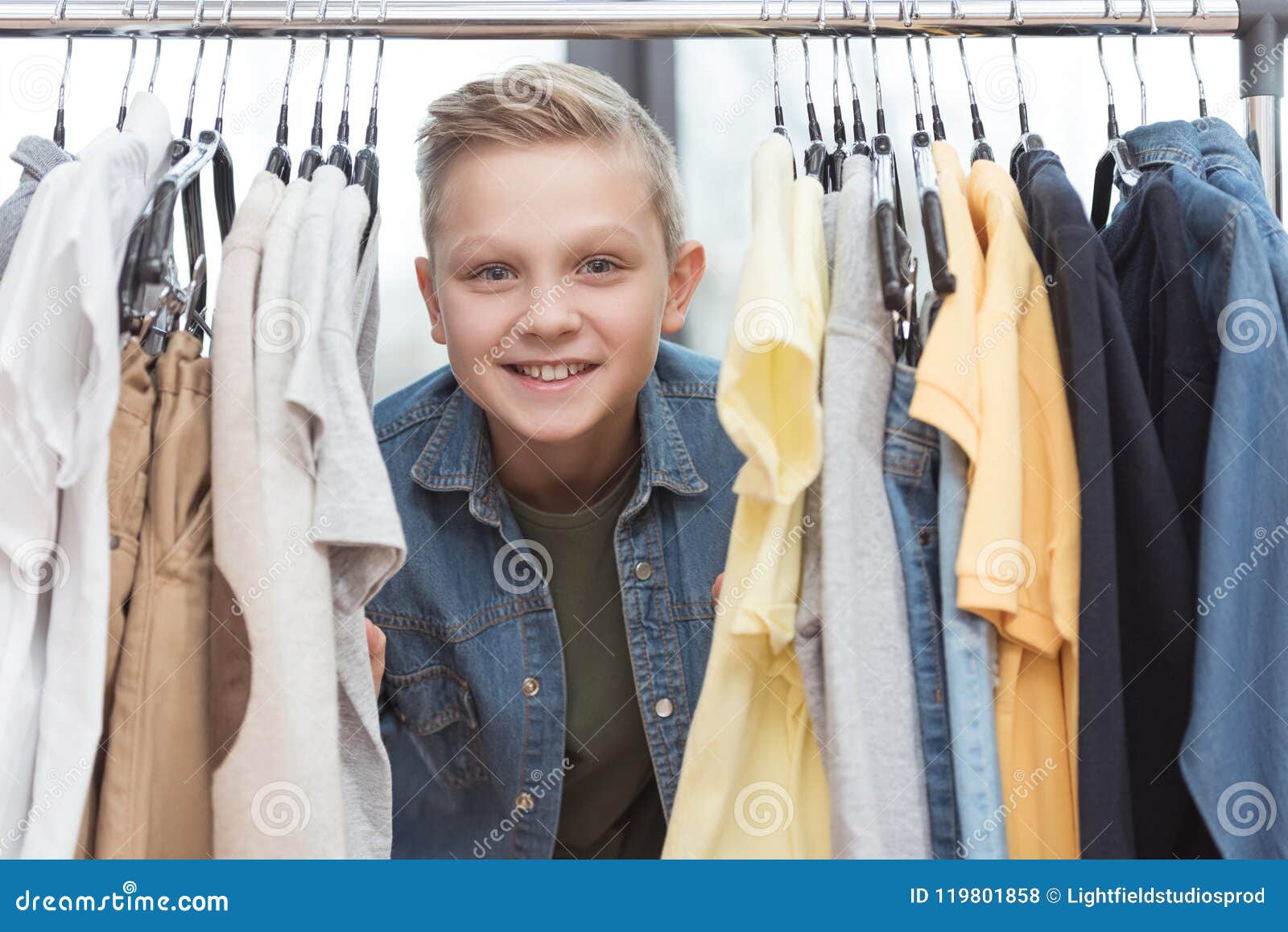 Smiling Boy Looking at Camera Surrounded by Clothes on Hanger Stock ...