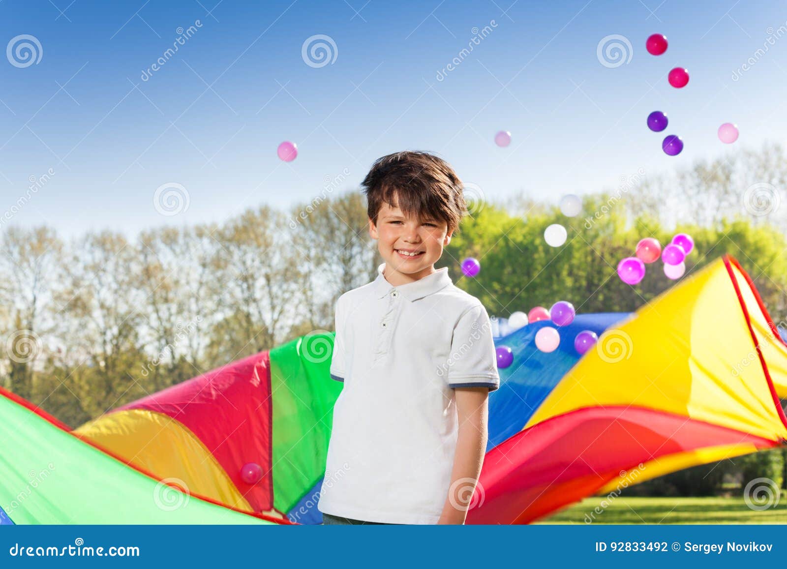 smiling boy playing rainbow parachute in the park