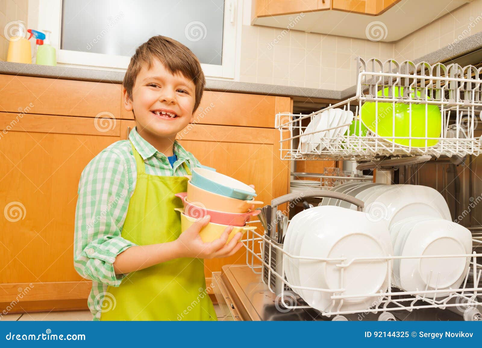 smiling boy pulling out bowls of the dishwasher