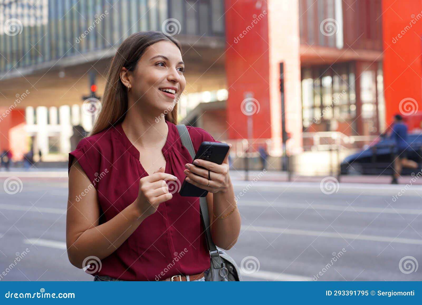 smiling brazilian woman hail a vehicle using mobile app waiting for taxi or uber on paulista avenue, sao paulo, brazil