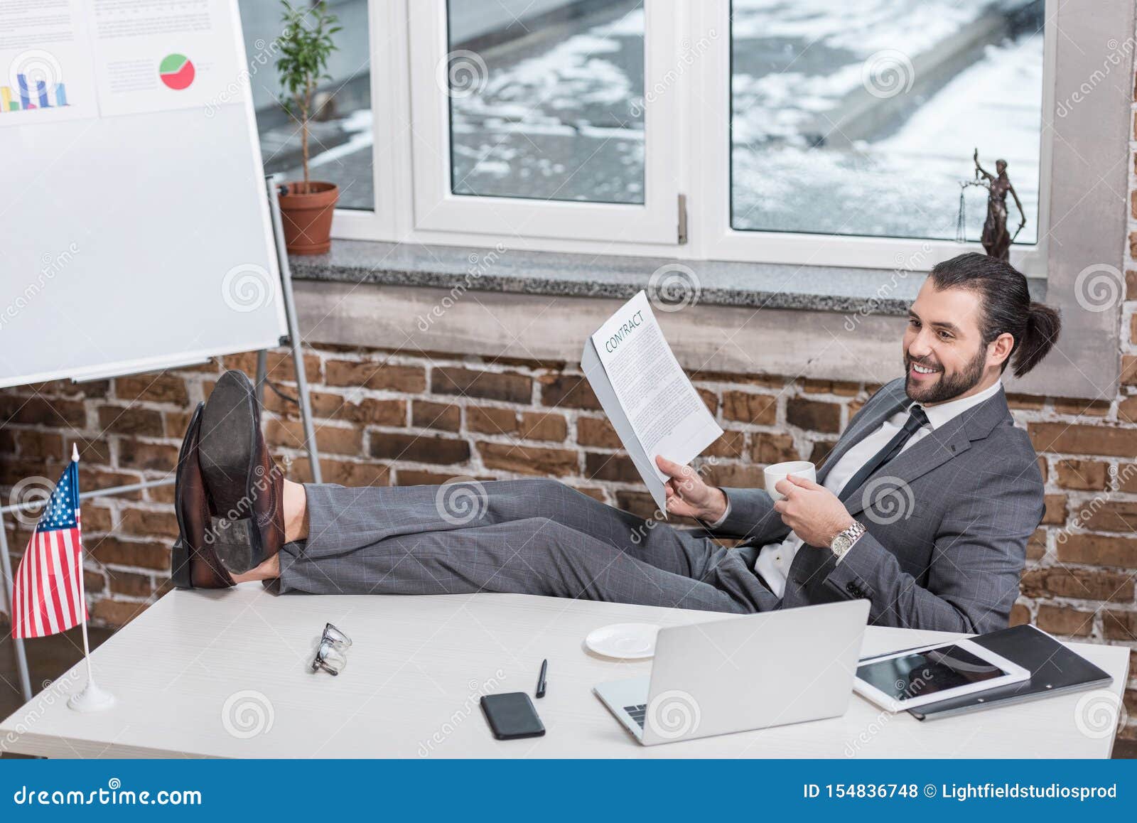 Smiling Businessman Sitting at Table and Putting Feet Up Stock Photo