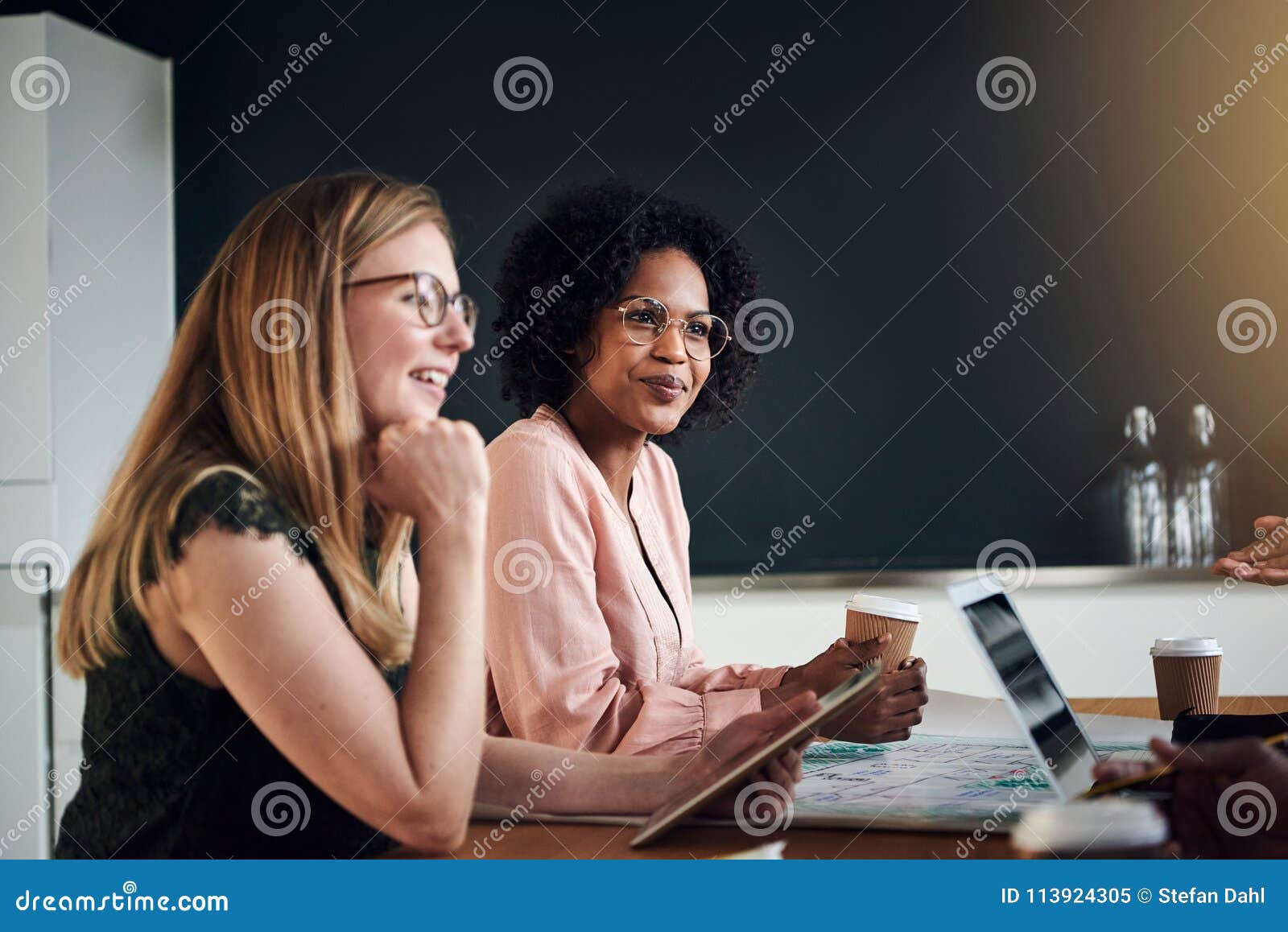 smiling businesswomen talking with colleagues in an office board