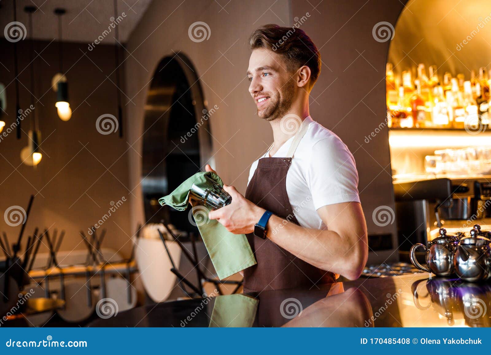 Smiling female bartender wiping glass with towel. Woman barista at