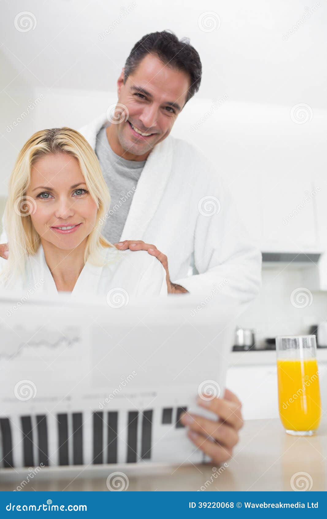 Smiling Couple in Bathrobes Reading Newspaper in Kitchen Stock Photo