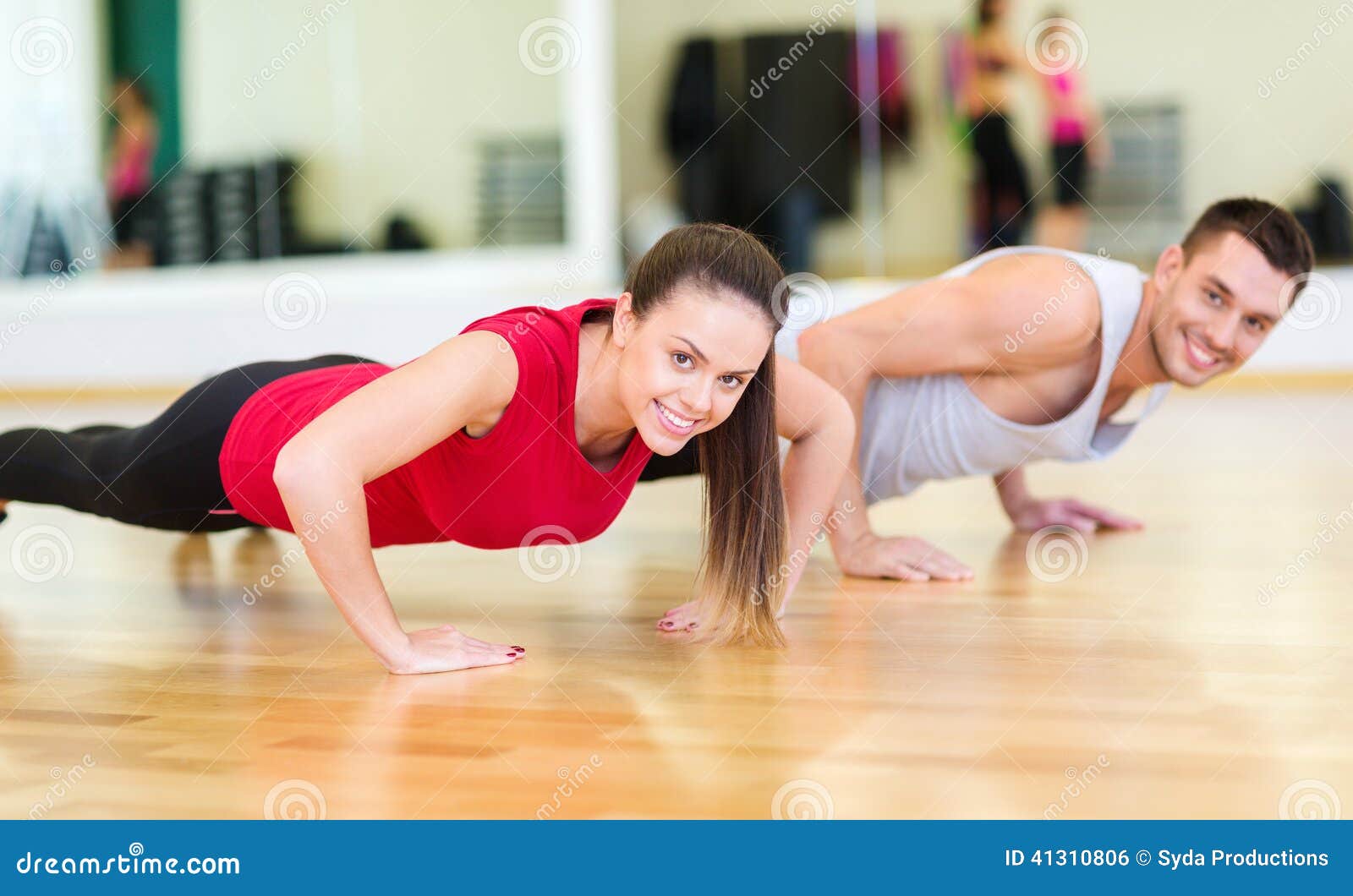 smiling couple doing push-ups in the gym