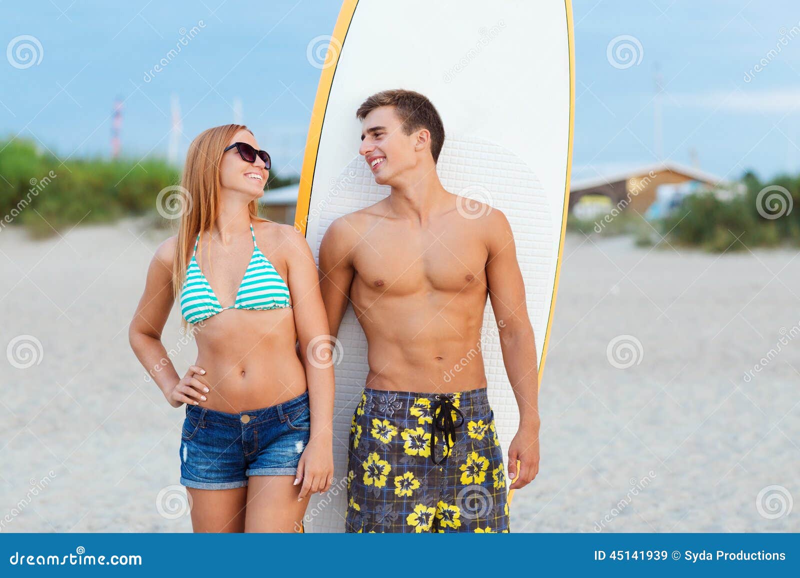 smiling couple in sunglasses with surfs on beach