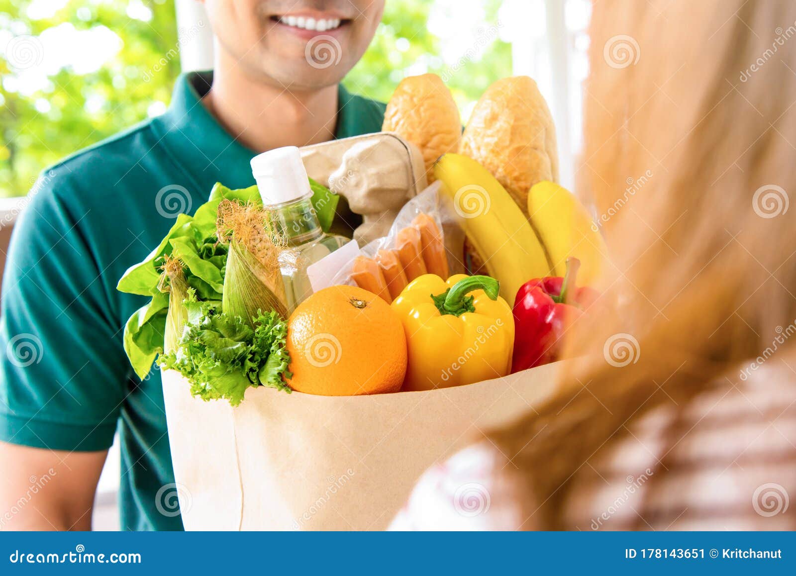 smiling delivery man giving grocery bag to woman customer at home