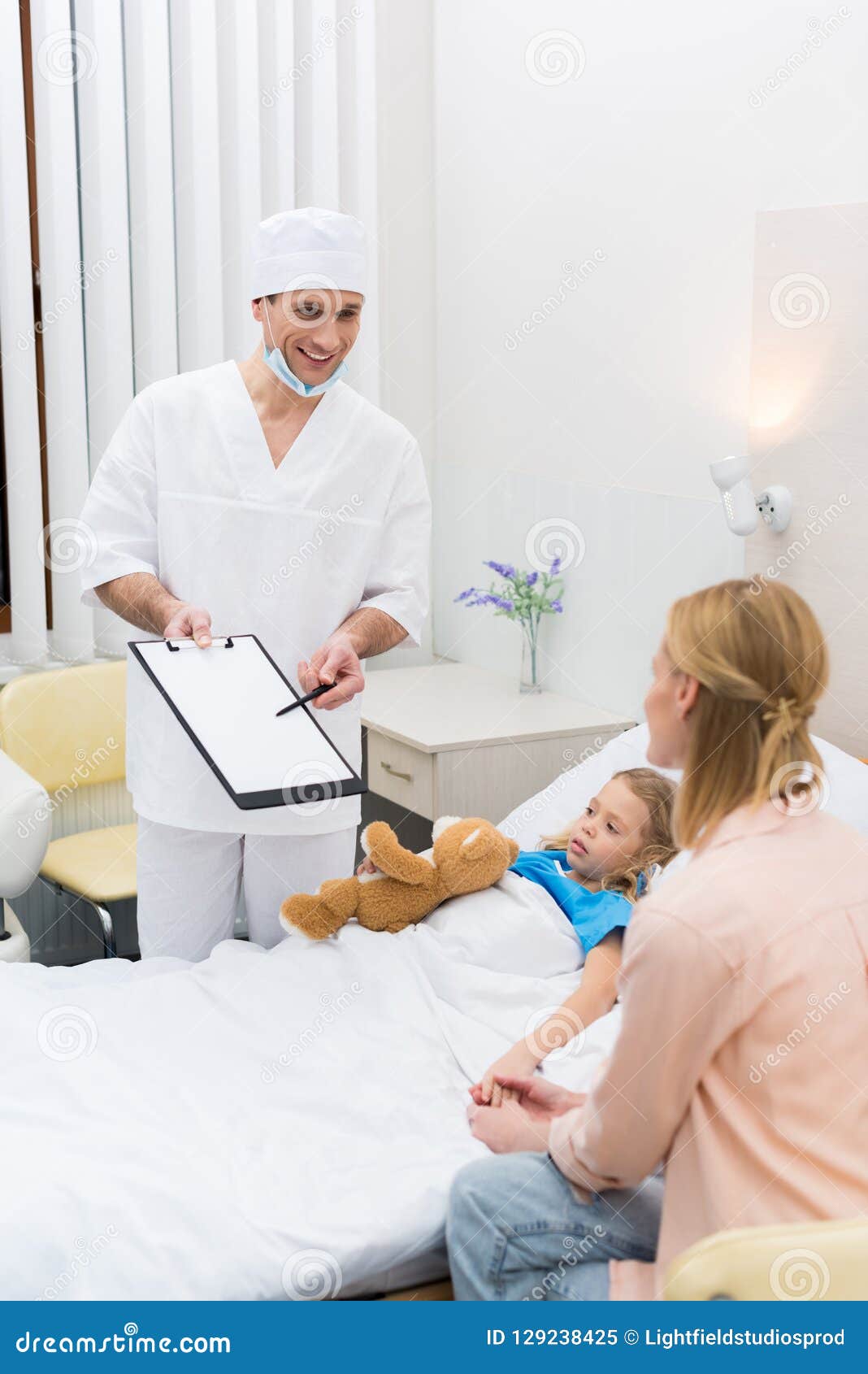 smiling doctor pointing on clipboard and talking with mother
