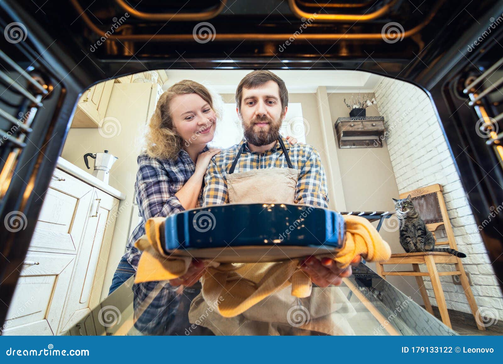 Smiling Eastern European Couple Cooking at Home and Taking Out a Pie