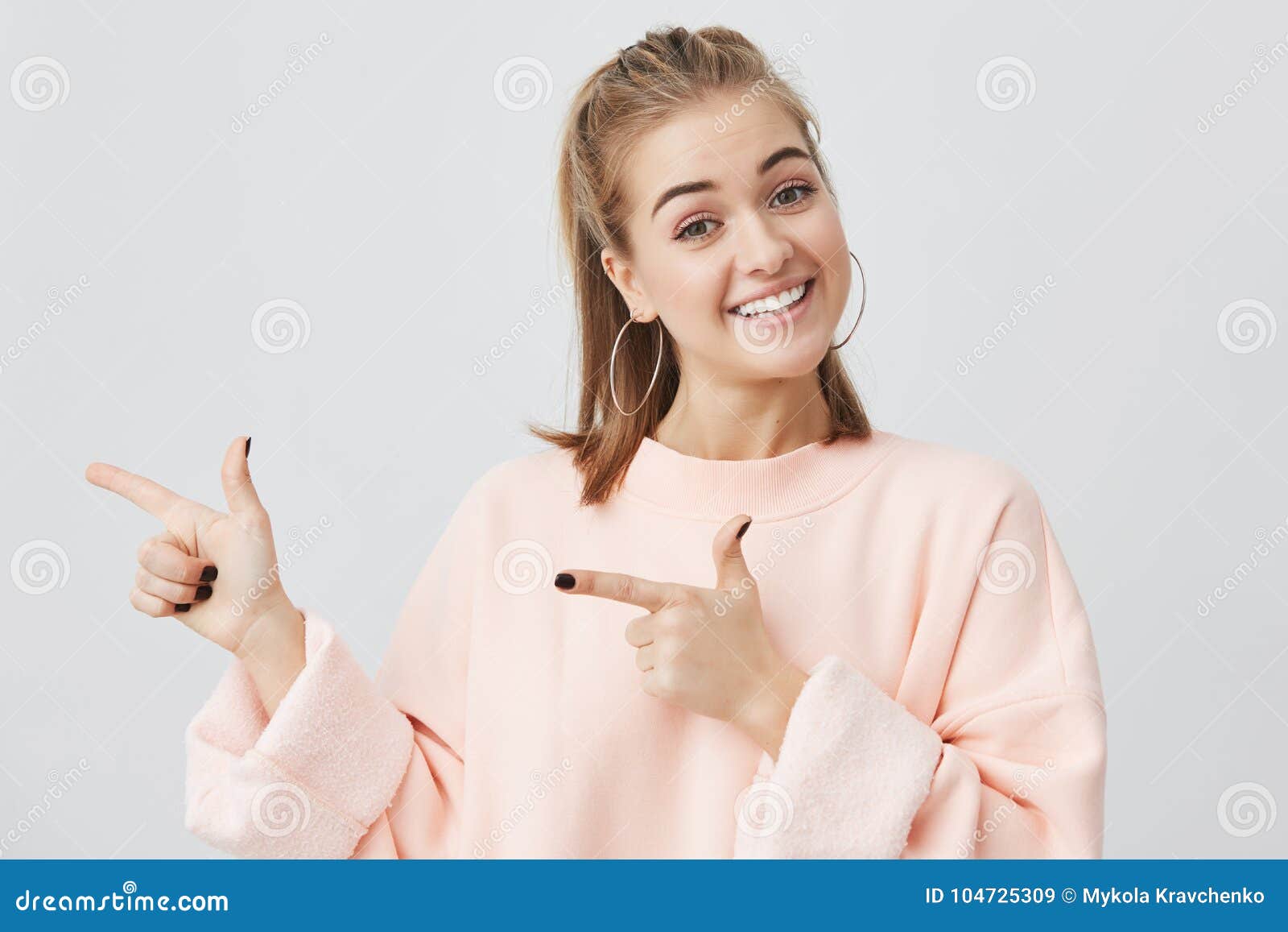 smiling fair-haired young woman in pink sweatshirt pointing at copy space for your advertisment or text. positive girl