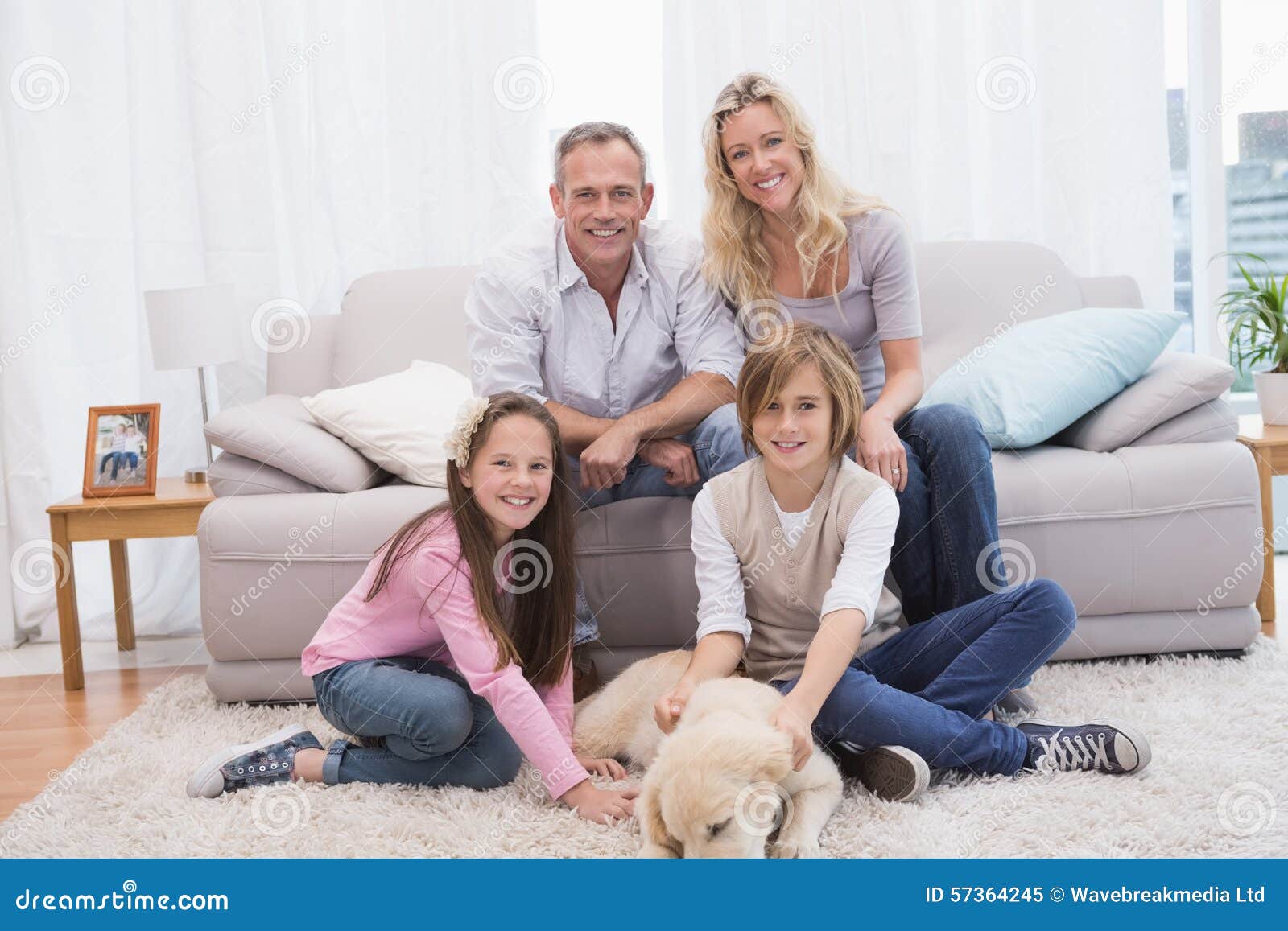 Smiling family with their pet yellow labrador on the rug at home in the living room