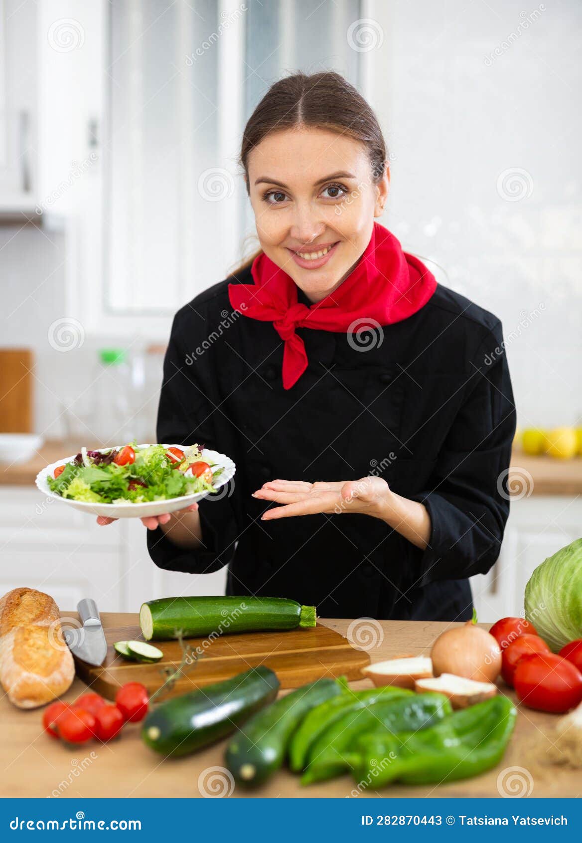 Smiling Female Chef in Black Uniform Offering Plate of Vegetable Salad