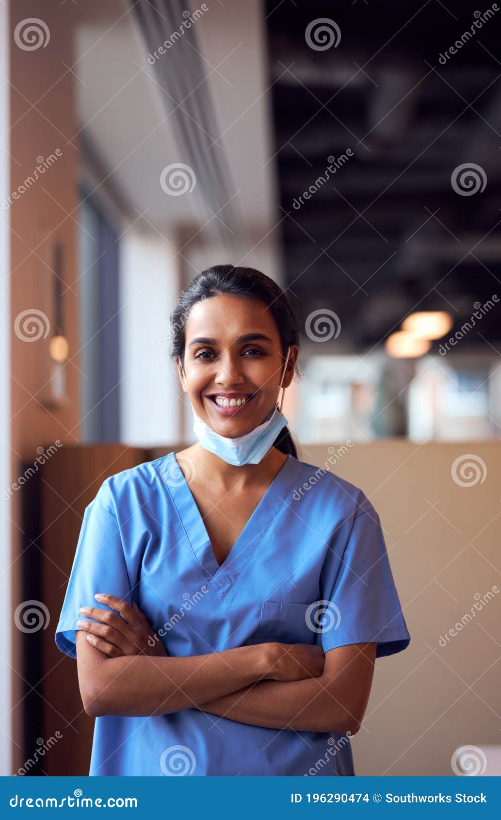 smiling female doctor with face mask wearing scrubs in busy hospital during health pandemic
