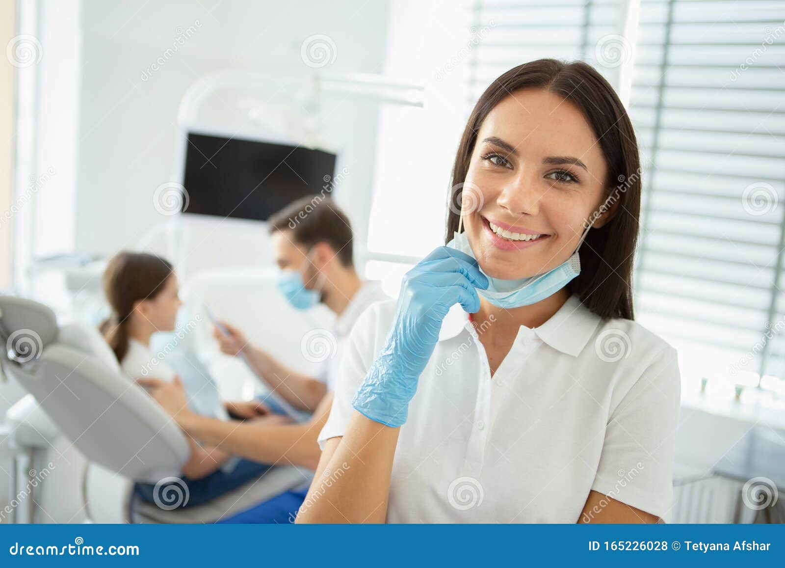 smiling female doctor showing looking at the camera while her collegue working with girl in dental chair on the background
