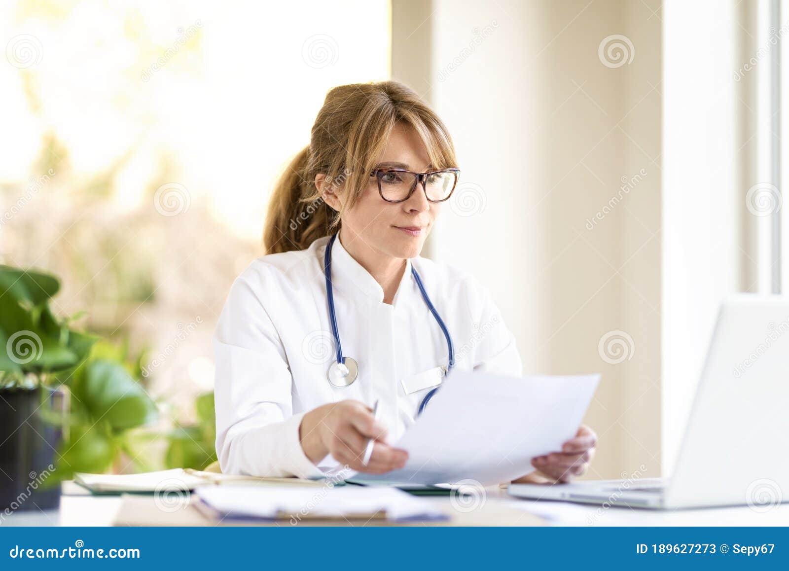 smiling female doctor sitting at desk and working on laptop