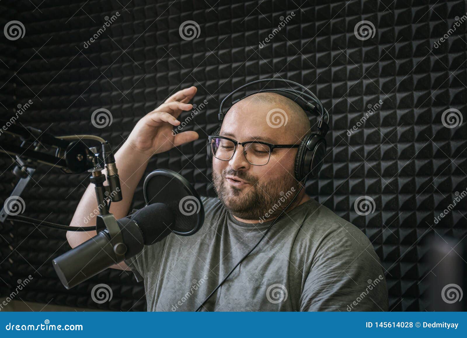 smiling and gesturing radio host with headphones on his head reading news from paper into studio microphone on radio station