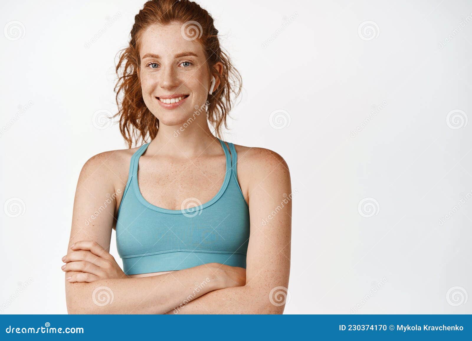 smiling ginger female athlete in sportsbra, cross arms on chest, looking determined and happy, workout in gym, standing