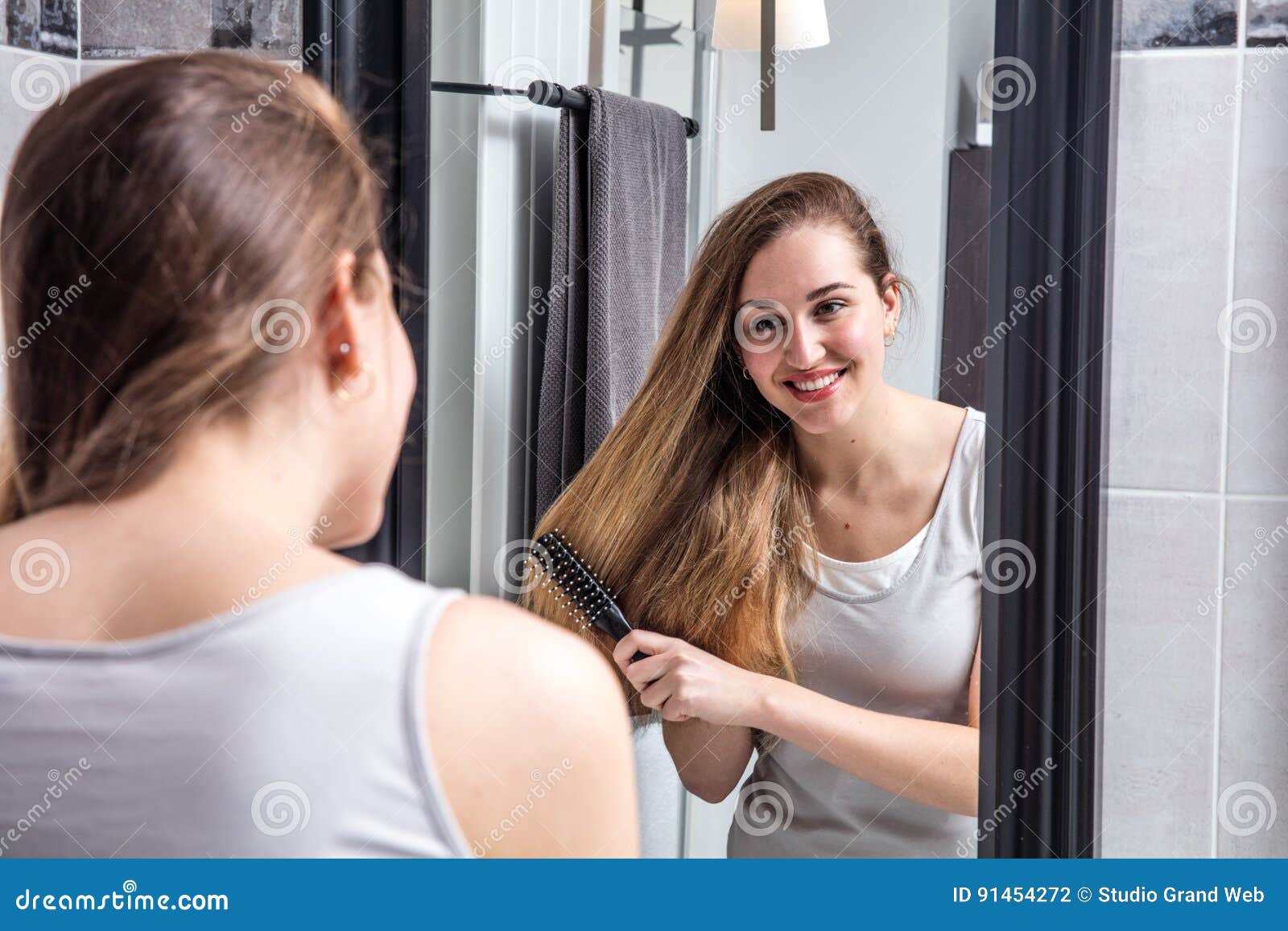 Smiling Girl Brushing Her Long Hair In Front Of Mirror Stock Photo