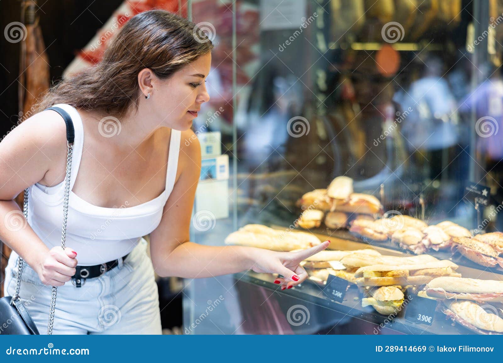 smiling girl choosing bocadillos in glass showcase of spanish street cafe