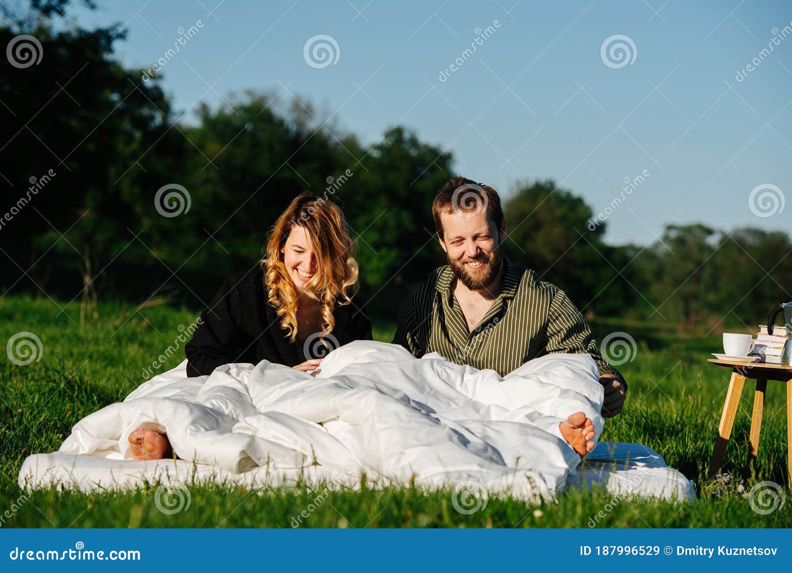 smiling groggy couple waking up from a nap in bed made outside in a countryside