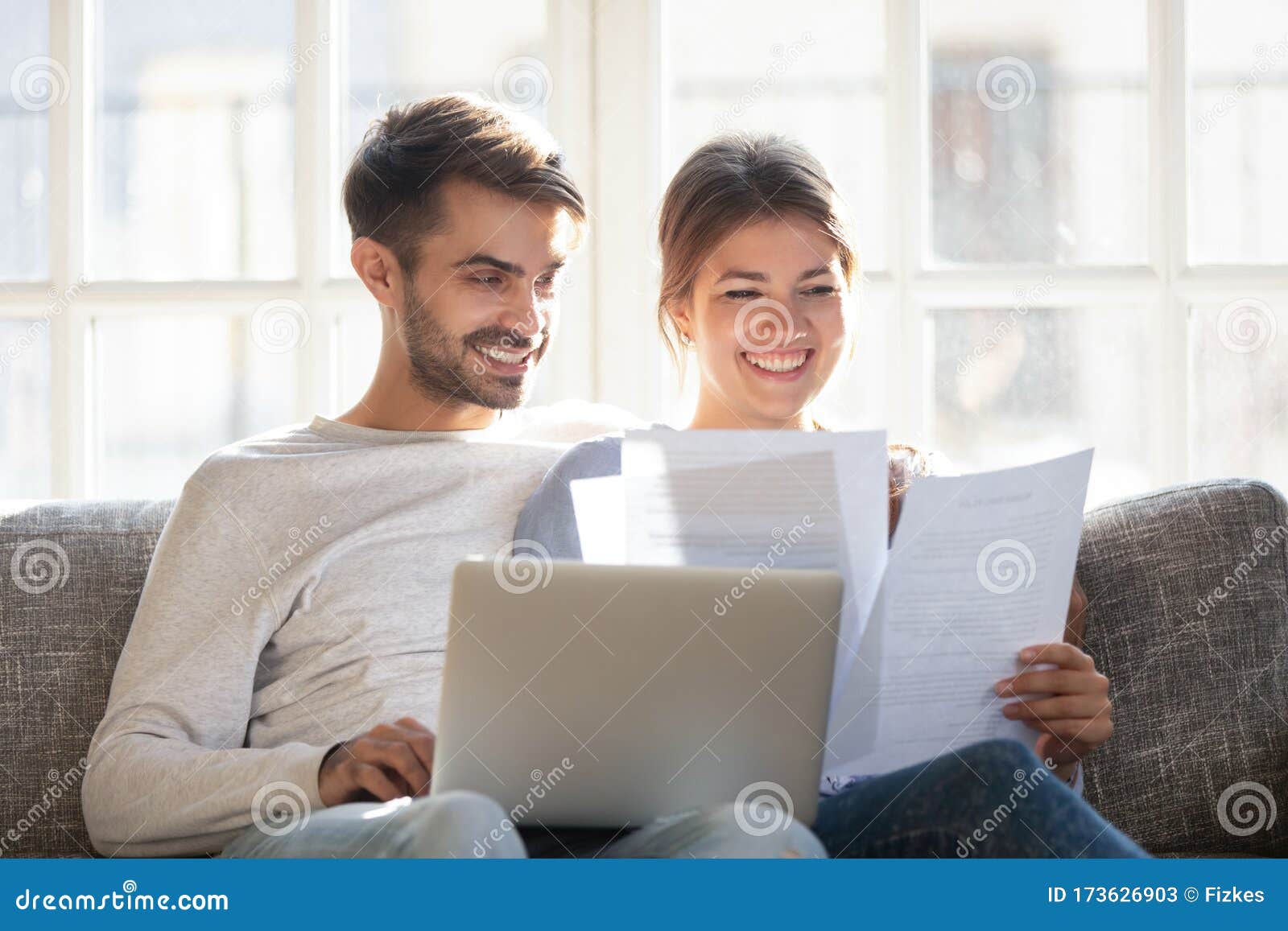 smiling couple hold paperwork paying bills online