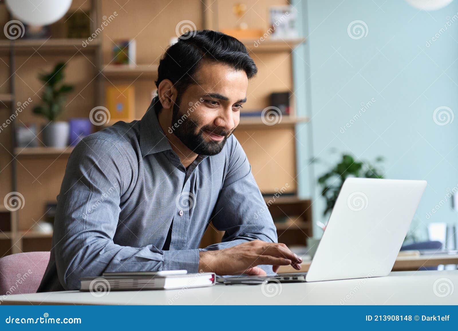 smiling indian business man working studying on laptop computer at home office.