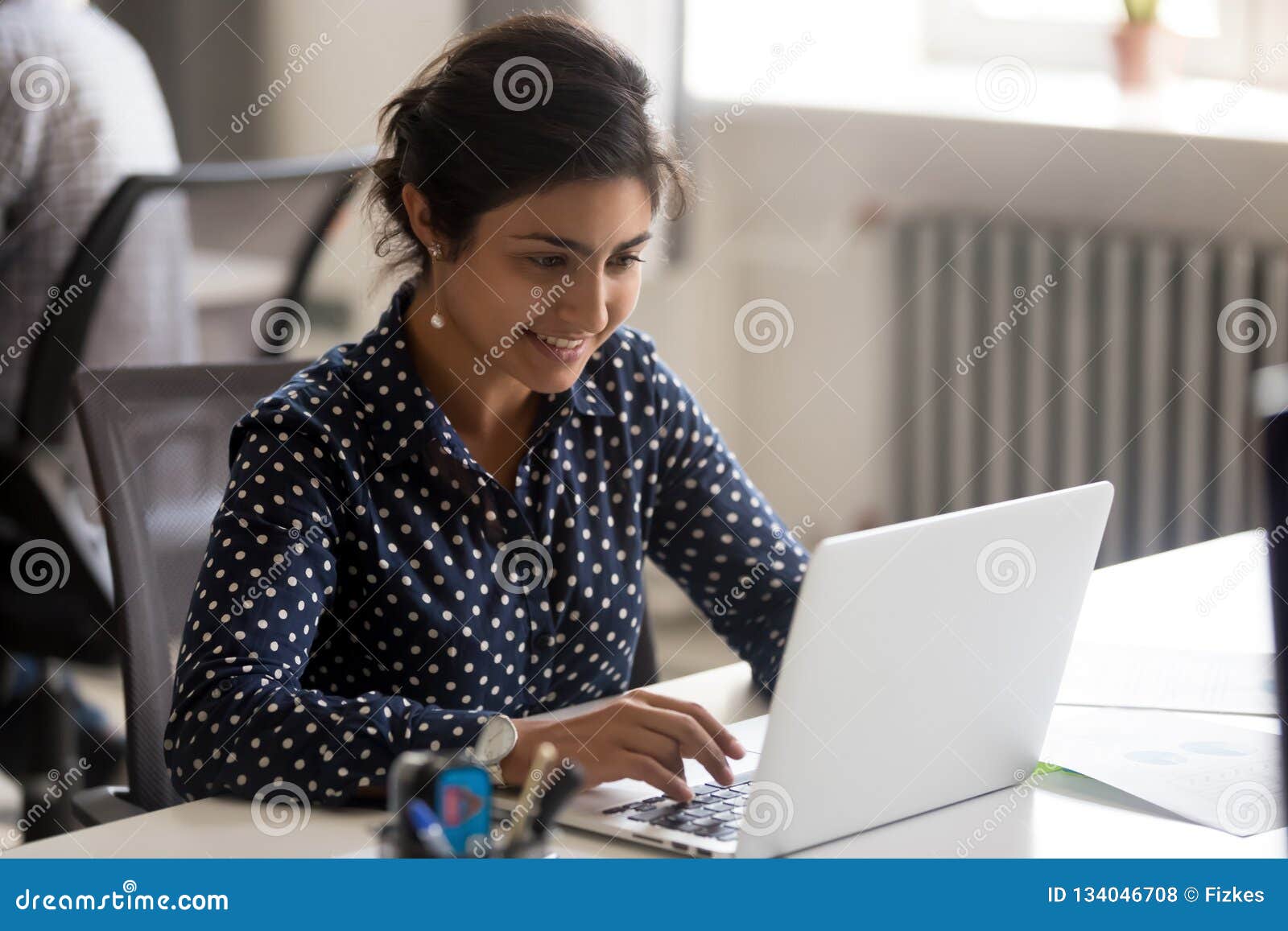 smiling indian female employee using laptop at workplace