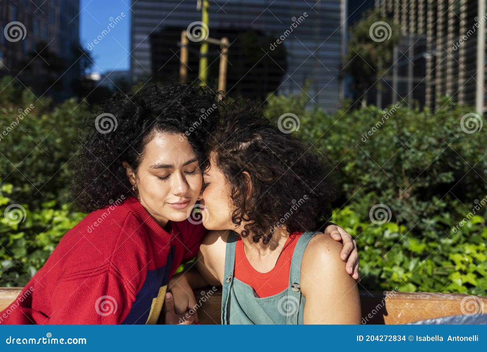 Smiling Lesbian Couple Embracing and Relaxing on a Park Bench Stock