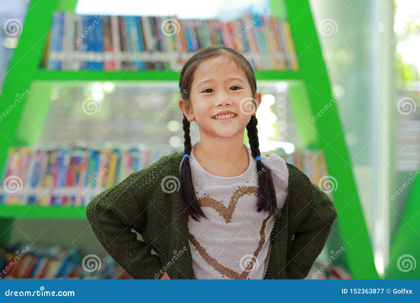 Smiling Little Asian Child Girl Against Bookshelf At Library