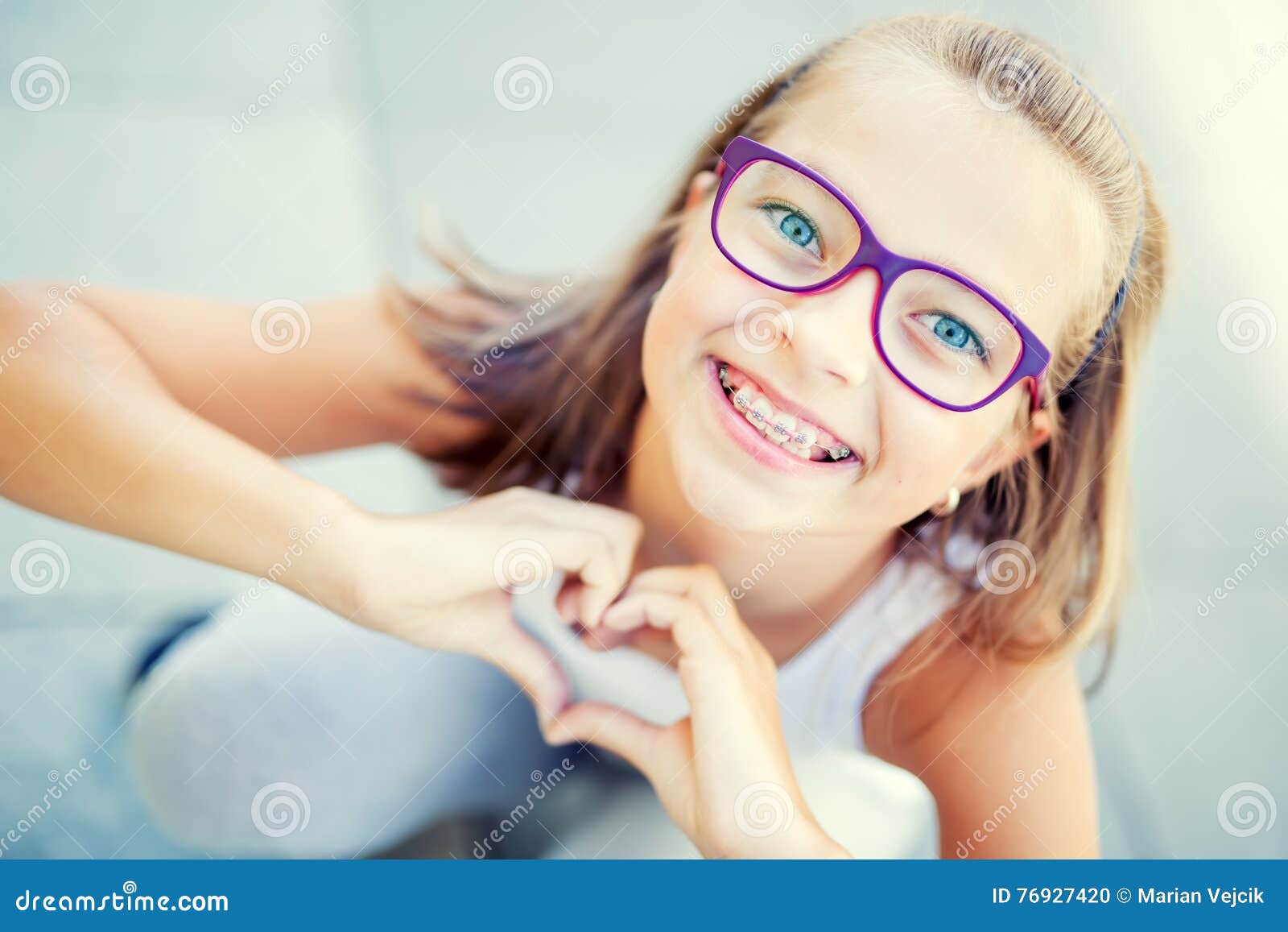 smiling little girl in with braces and glasses showing heart with hands