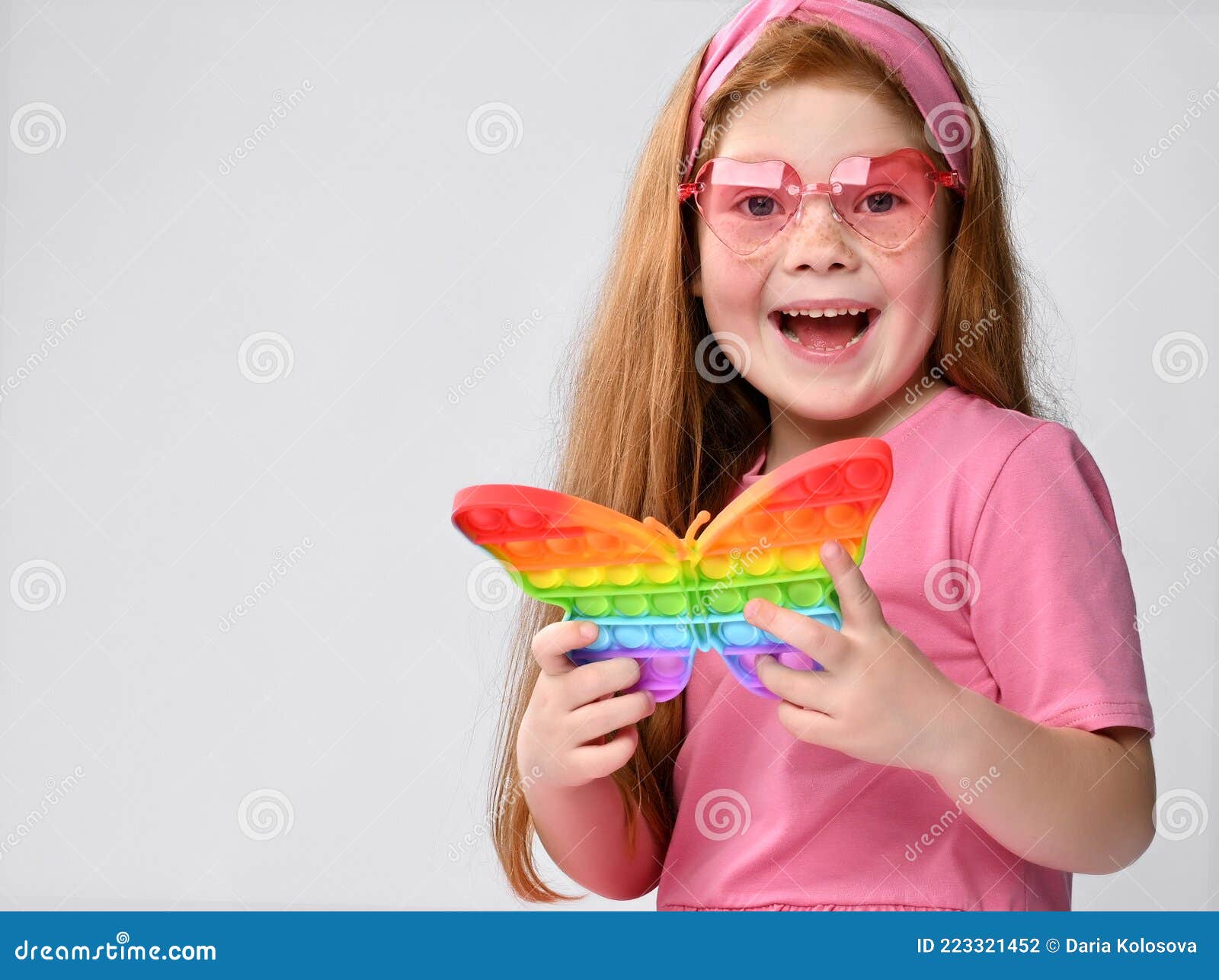smiling little red-haired girl child playing with pop it toy studio shot