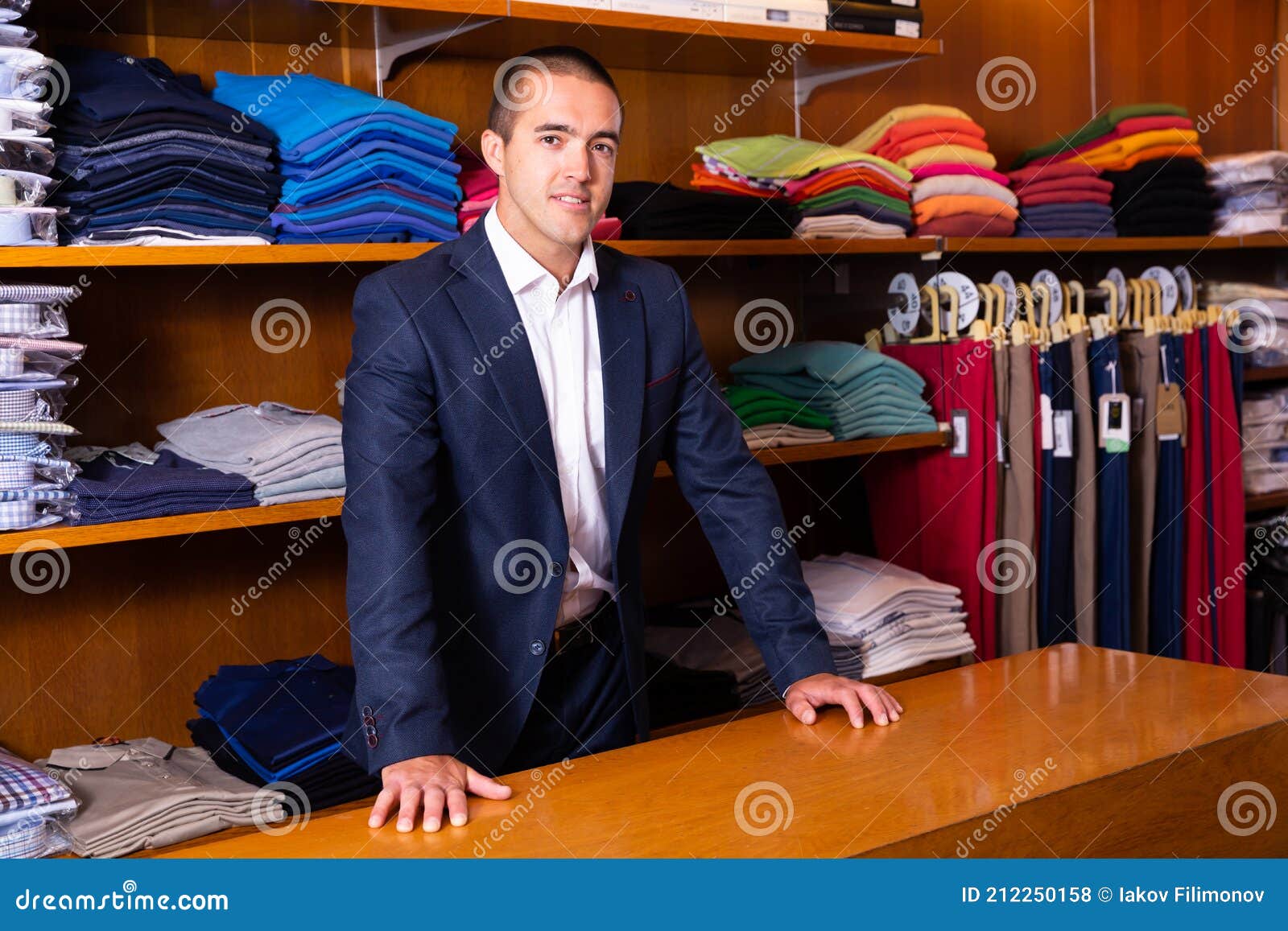 smiling male seller demonstrating shirts to customer in men cloths store