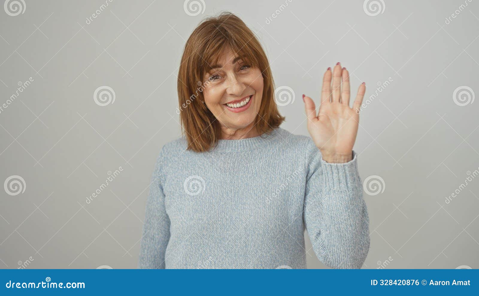 smiling middle-aged woman in a sweater greeting with handwave against a white background