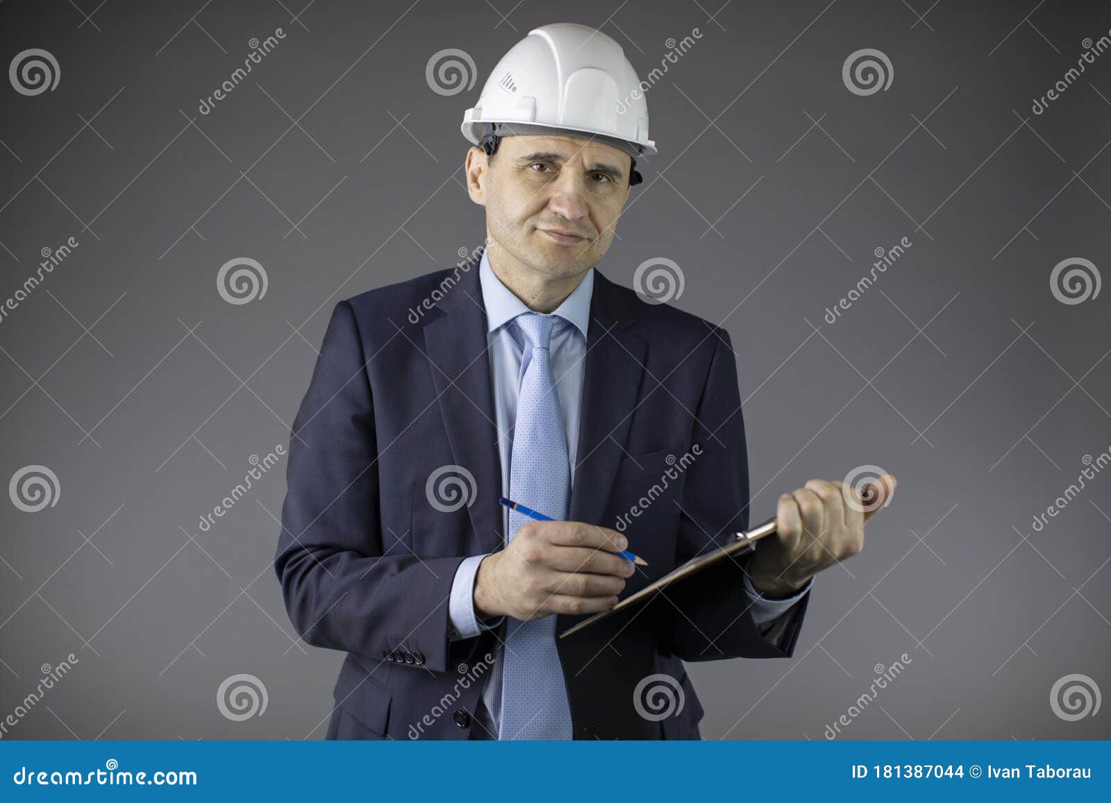smiling mining engineer in hard hat makes notes on clipboard and looks at camera