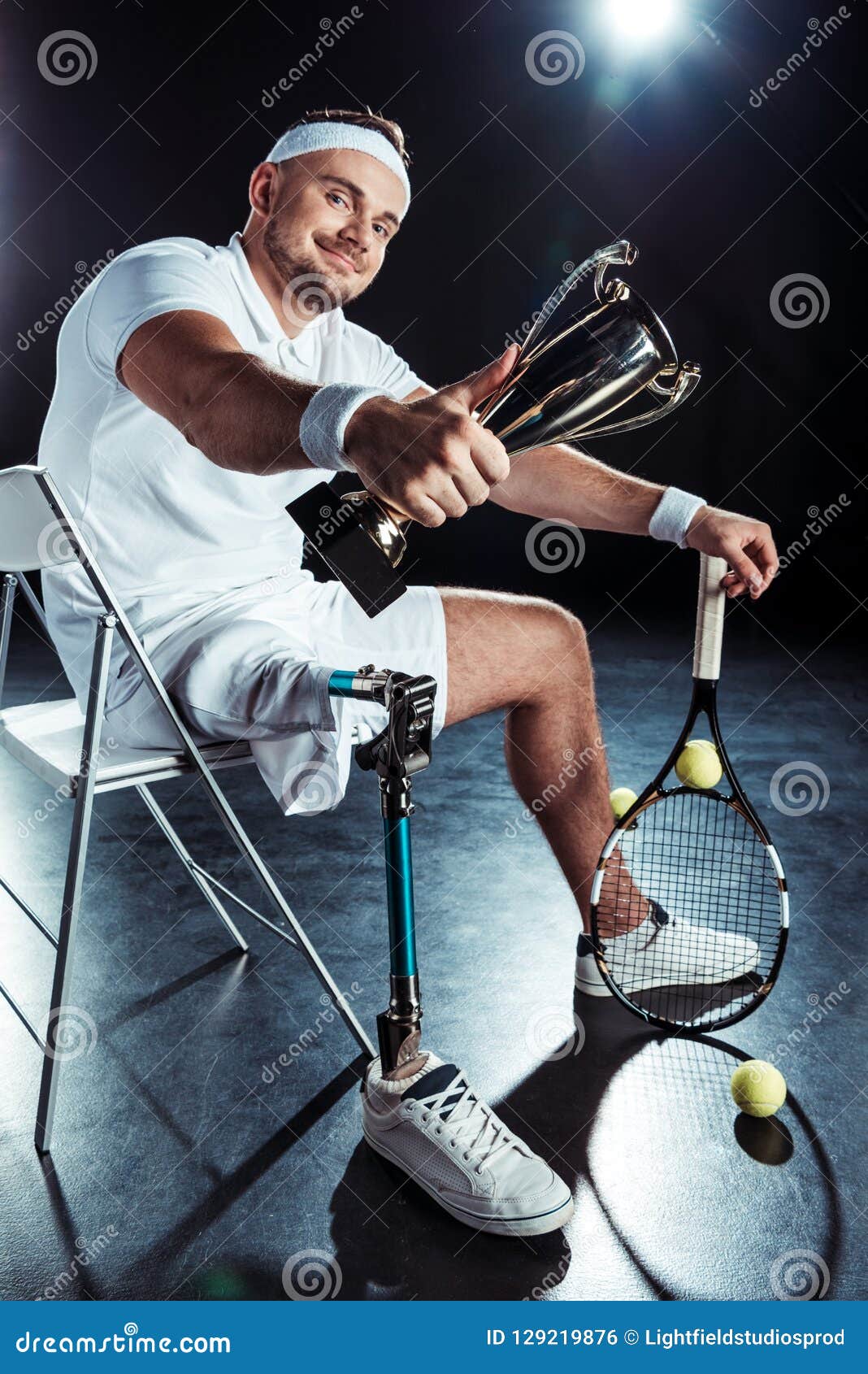 smiling paralympic tennis player showing champion goblet while resting