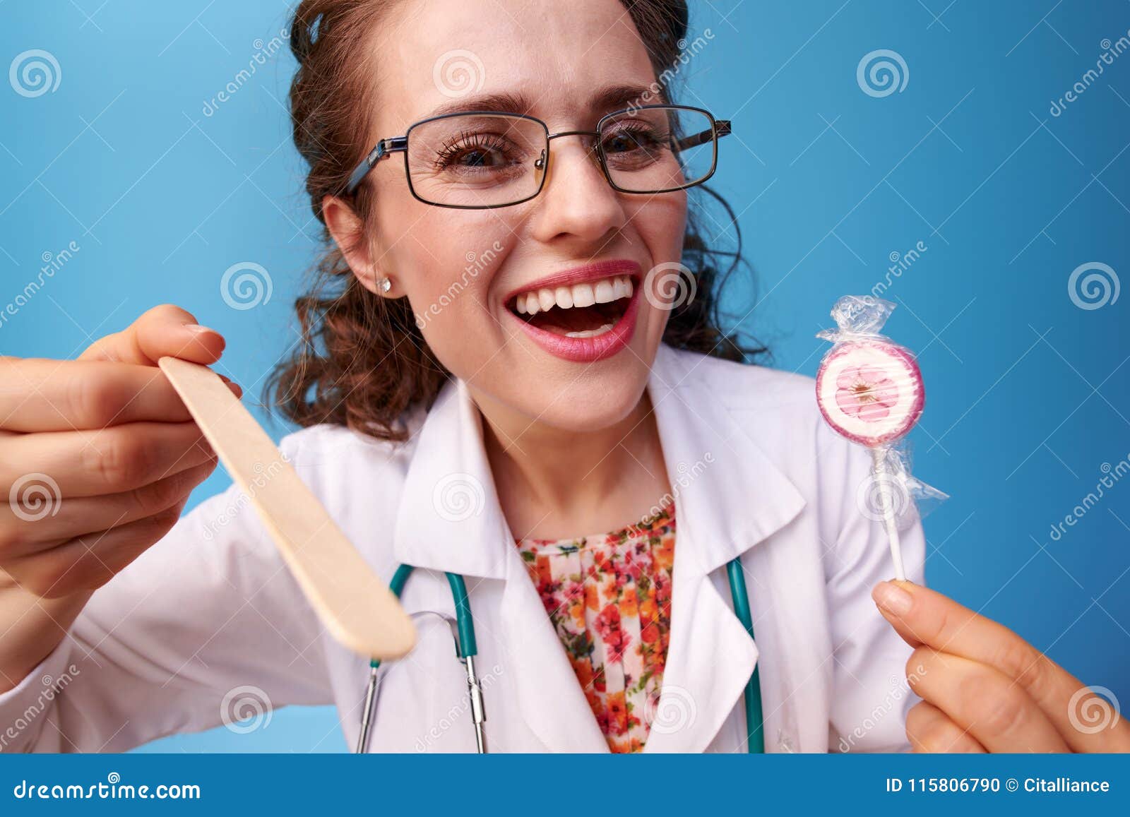pediatrist doctor with lollipop using spatula to examine throat