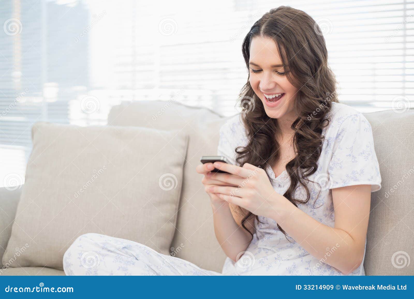 Smiling Pretty Woman in Pyjamas Reading a Text on Her Smartphone Stock ...