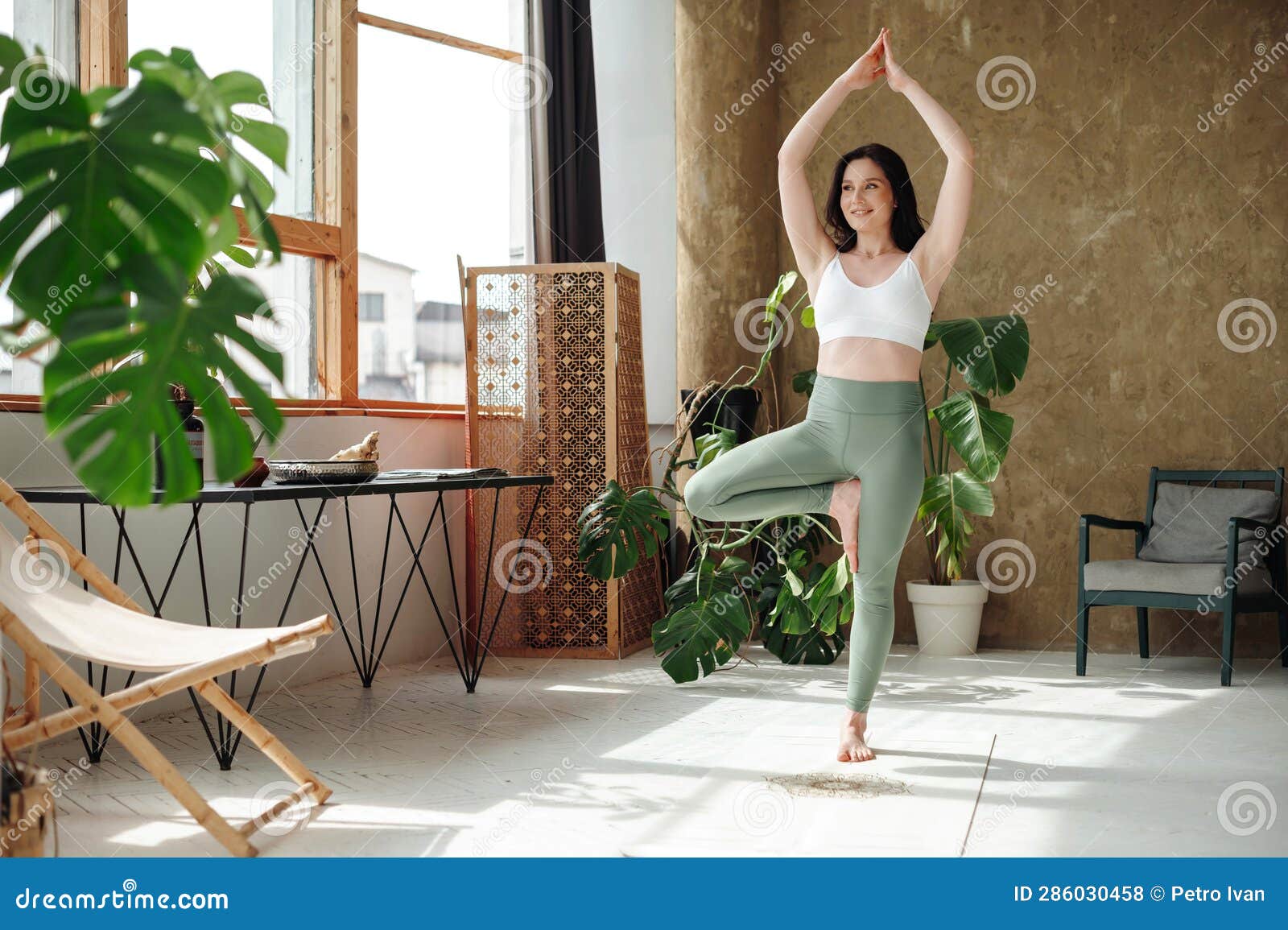 Fit Smiling Woman Practicing Tree Yoga Pose in Cozy Place Stock