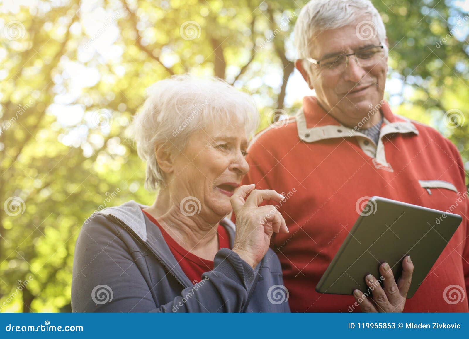 senior couple enjoying in park together and using digita