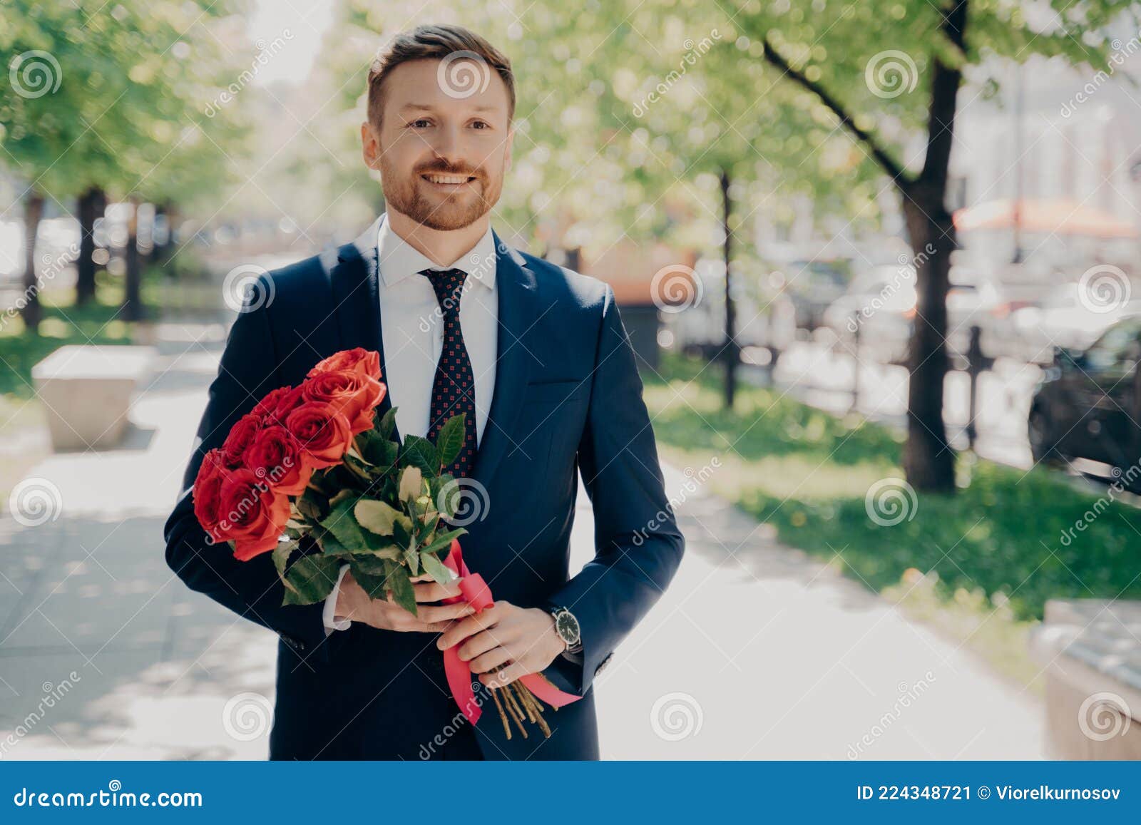 smiling stylish stubbly gentleman in dark blue tuxedo with big bouquet