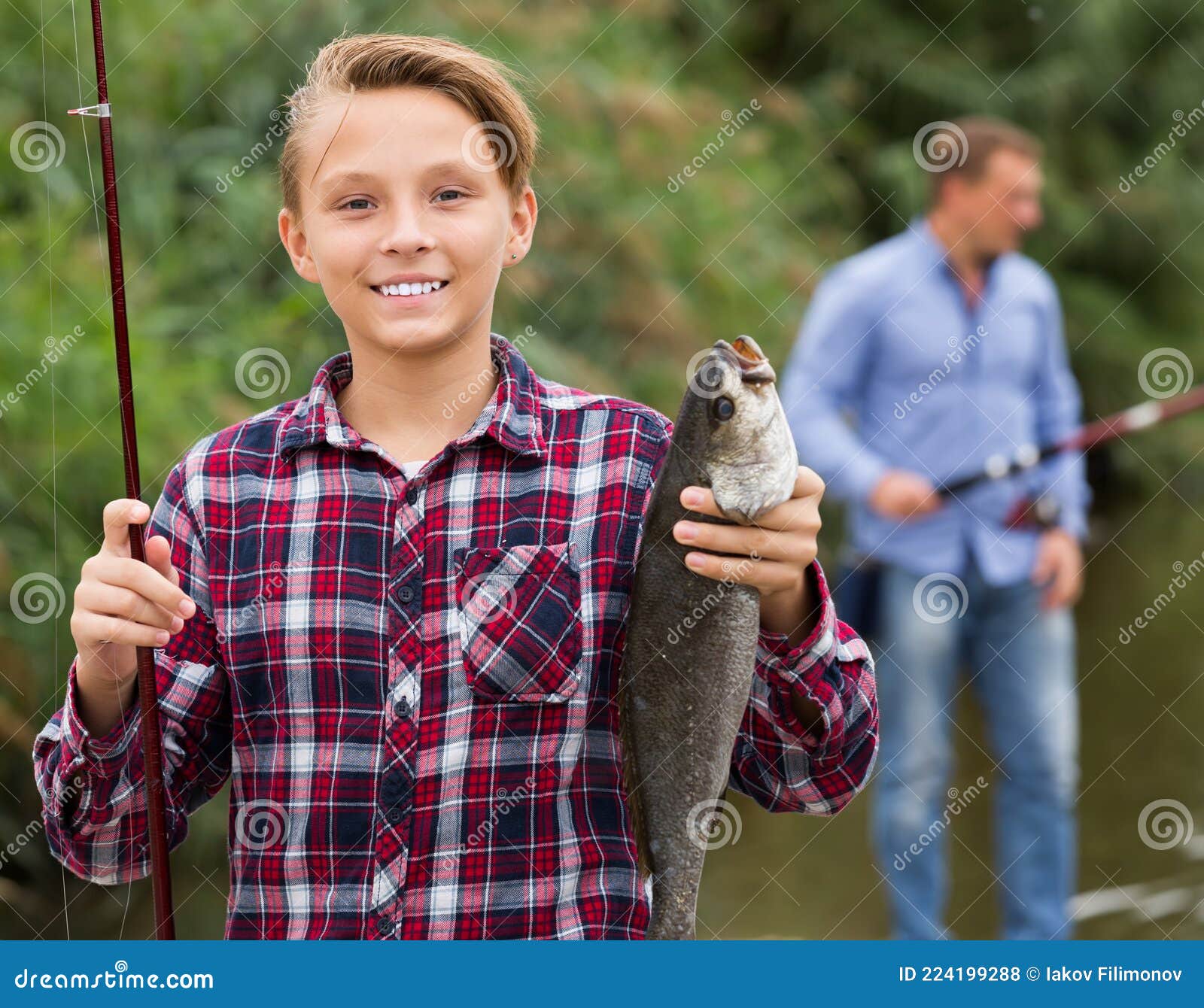 Smiling Teenage Boy Holding Catch Freshwater Fish In Hands Stock