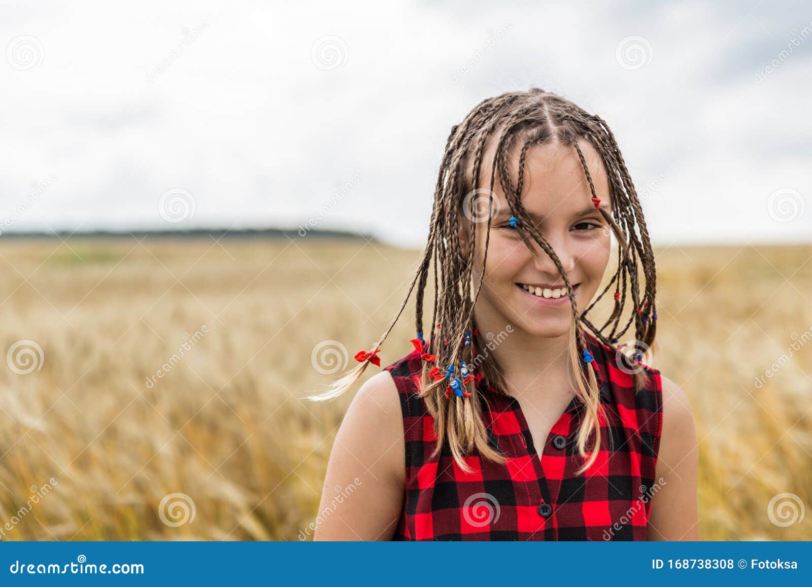 Smiling Teenage Girl With Braids Sitting In Wheat Field At 