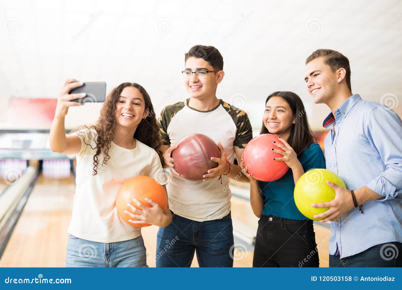 teens capturing memories of bowling on mobile phone in alley