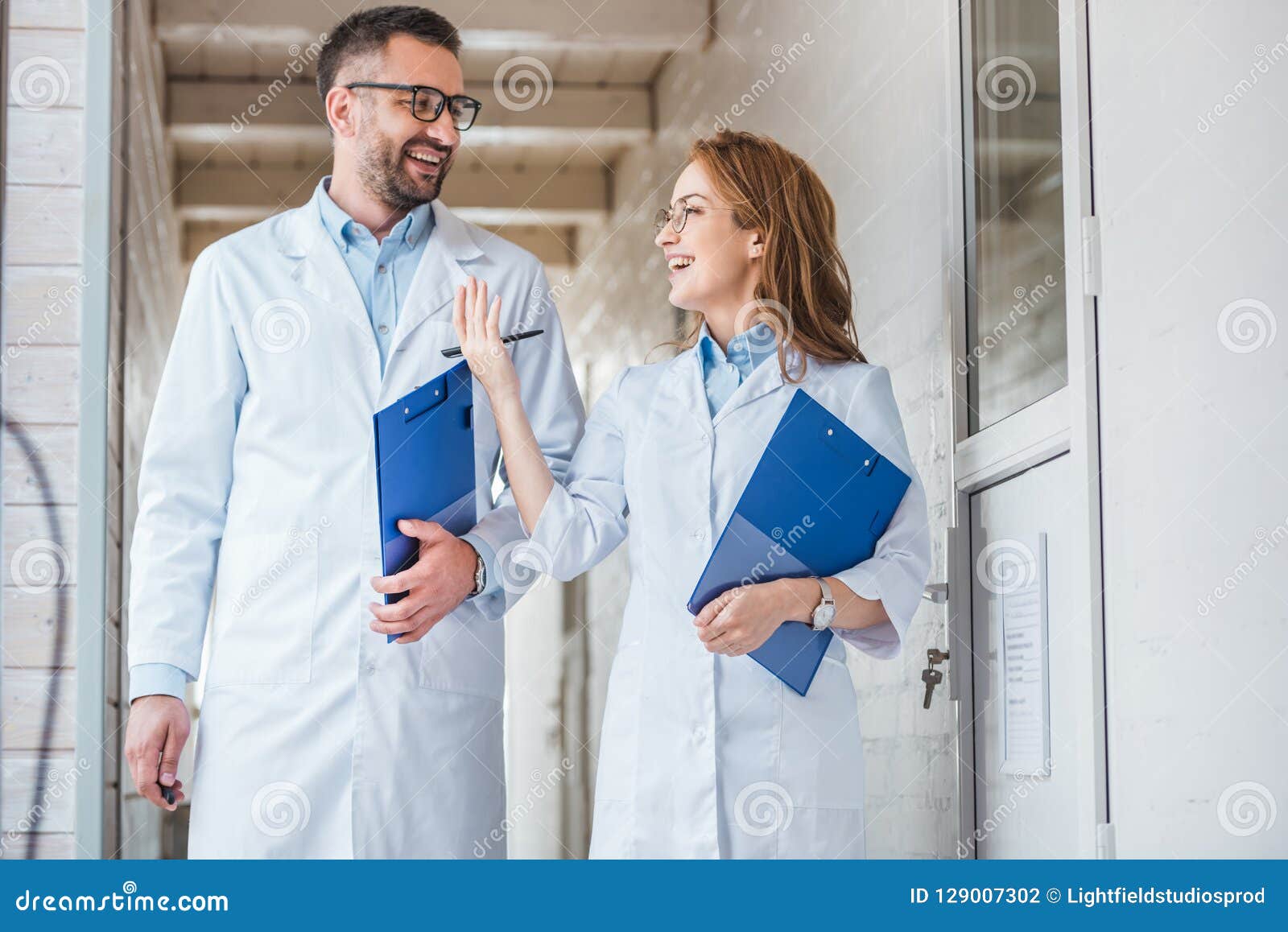 smiling vets in white coats walking with clipboards in veterinary clinic and looking at each other