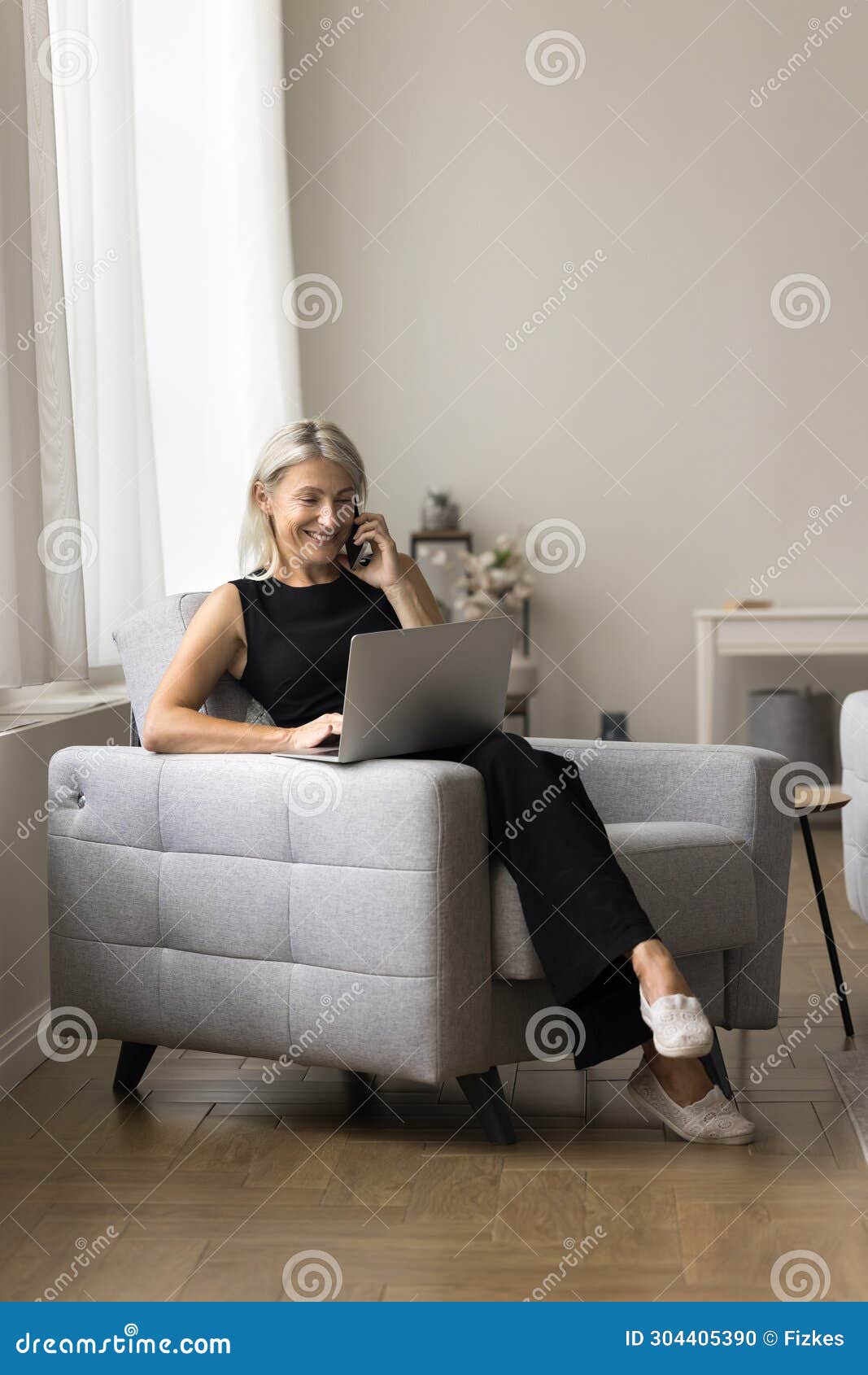 woman enjoy conversation on smartphone seated on armchair with laptop